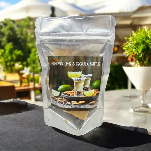 Bag of Almond Lime Tequila Brittle on outdoor patio with umbrellas, shrubs and cocktail